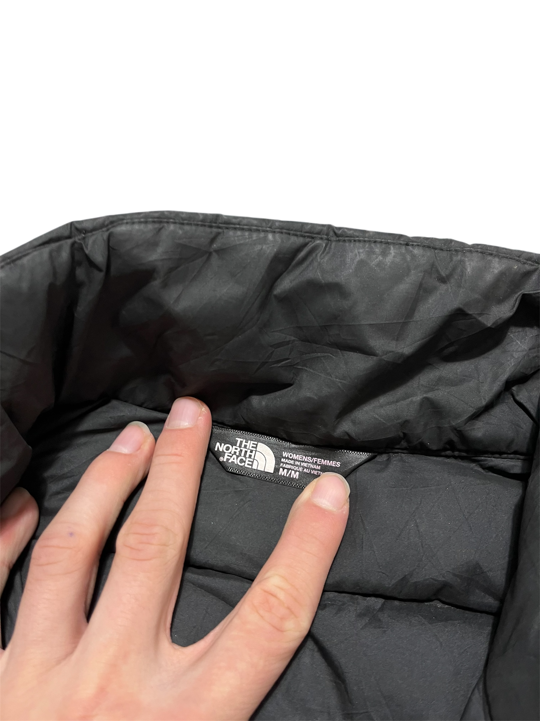The North Face fekete női kabát belső címkéje, kézzel tartva, streetwear divat